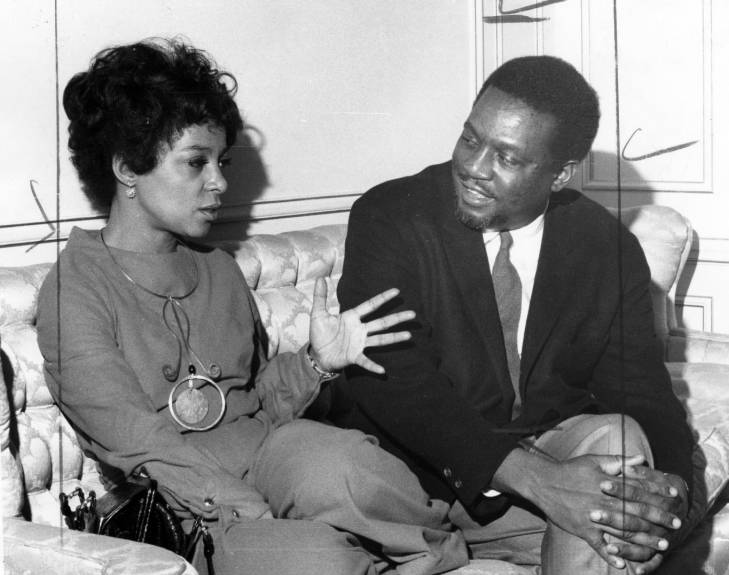 Ruby Dee and a man in a suit are sitting next to each other on a sofa and talking