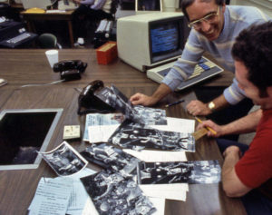 Two people working at a desk covered in black and white photographs