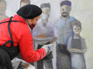Color photograph of local artist creating a chalk mural of service industry workers to show appreciation of their labor during the COVID-19 pandemic