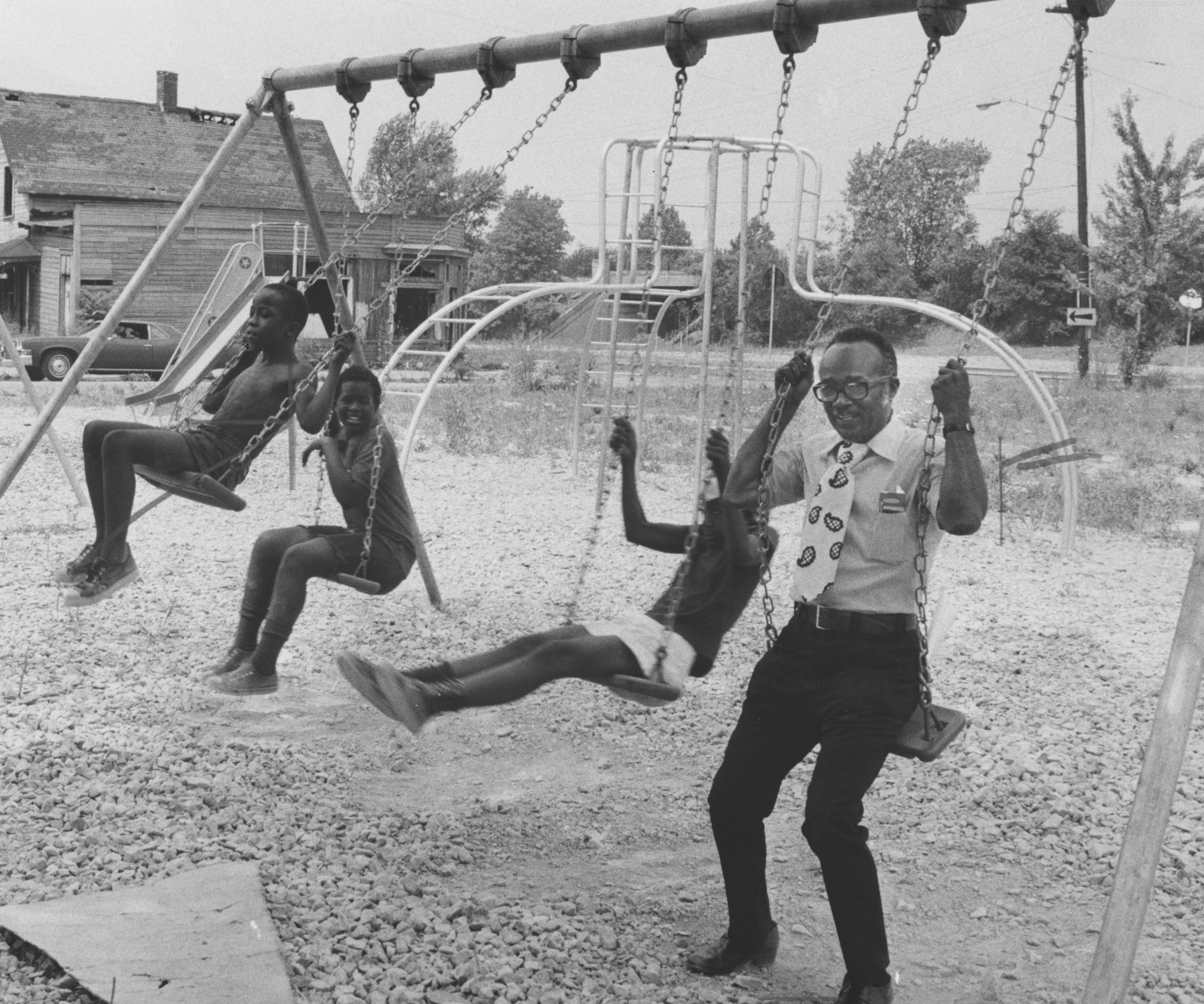 Black and white photograph of two boys and one man playing on a swing set