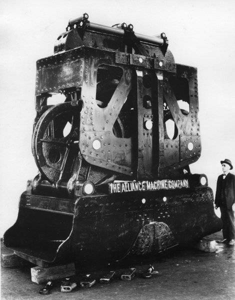 Black and white photograph of a man standing next to a large piece of mining equipment
